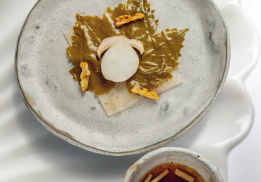 FEUILLE D’AUTOMNE : MAIGRE SERVI CRU, ASSAISONNÉ D’HUILE DE NOIX  ET JUS DE CITRON DE PROVENCE CACHÉ SOUS UNE FEUILLE DE VIGNE MARINÉE, CERNEAUX DE NOIX TORRÉFIÉS, BOUILLON DE CHAMPIGNONS BLANCS ET POISSONS DE ROCHE SÉCHÉS, COPEAUX DE CÈPE CRU