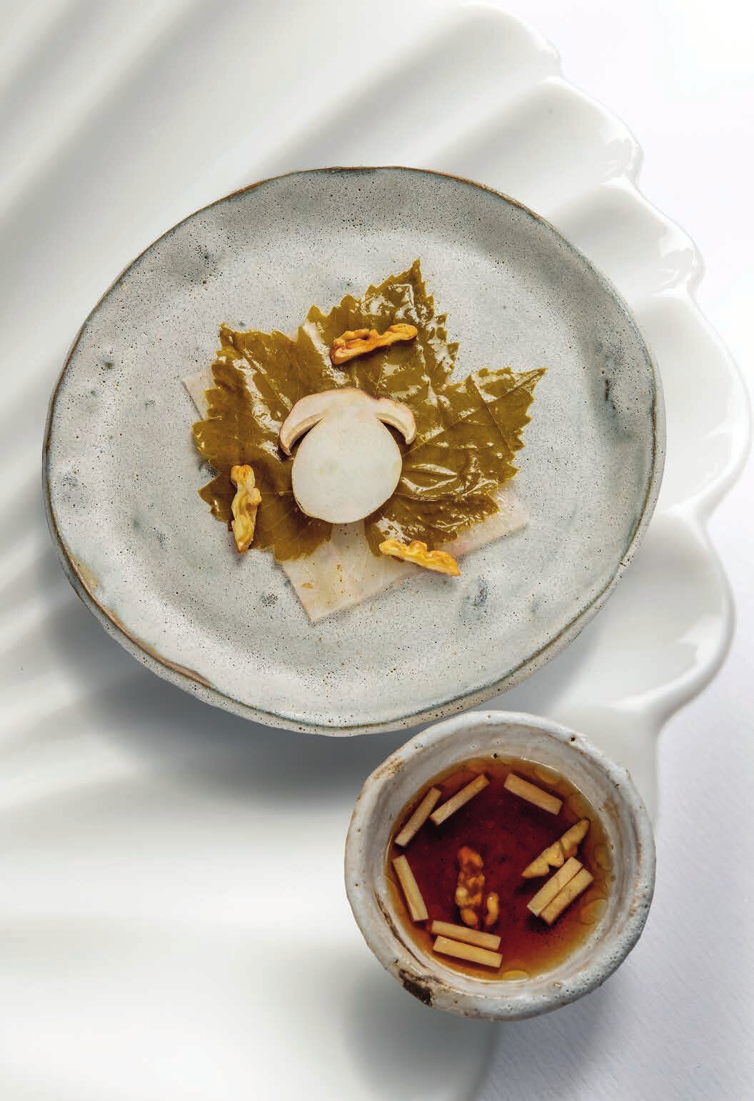 Feuille d’automne : maigre servi cru, feuille de vigne marinée, cerneaux de noix torréfiés, bouillon de champignons blancs et poissons de roche séchés, copeaux de cèpe